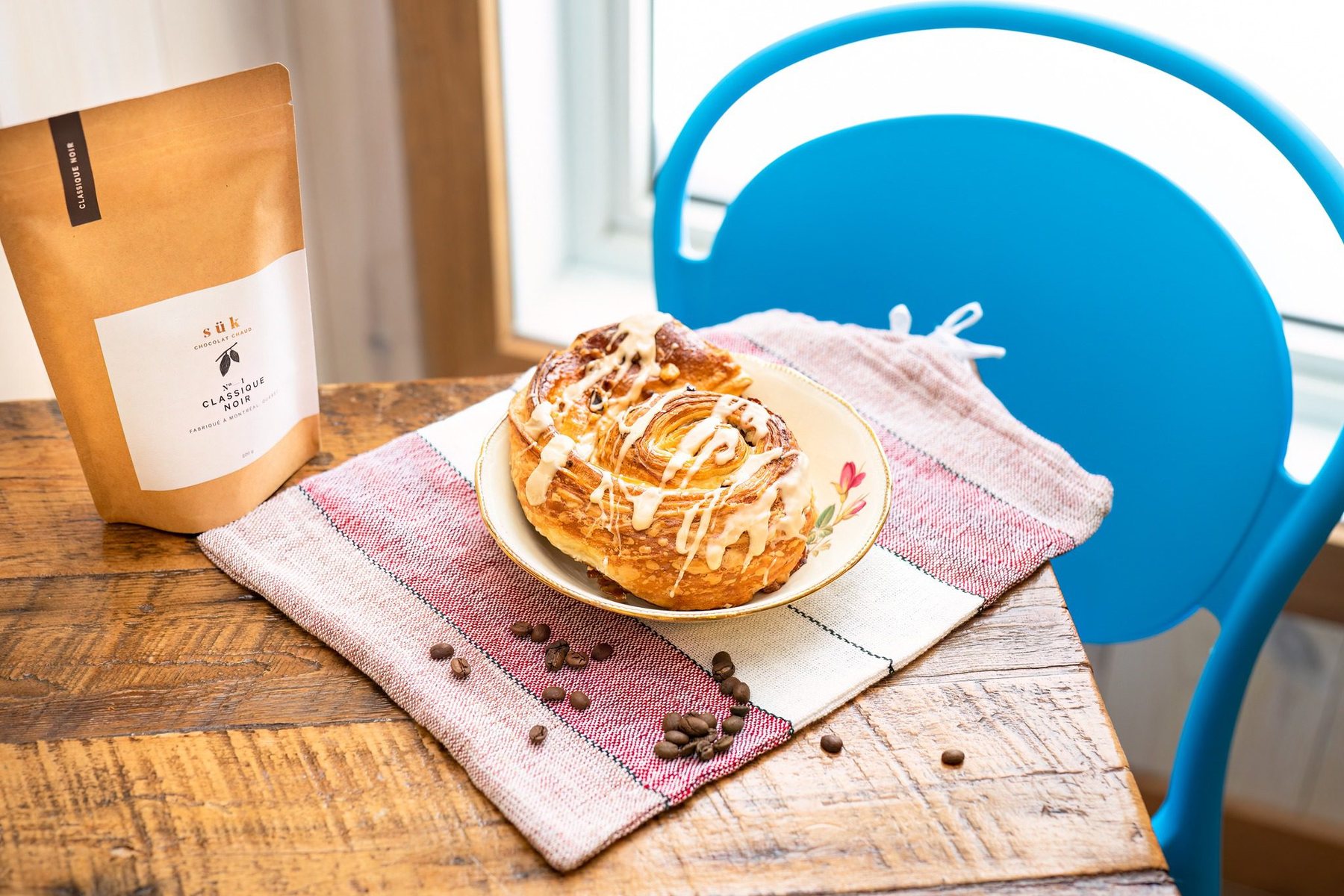 Un sac de café et une brioche glacée, sur une table de bois